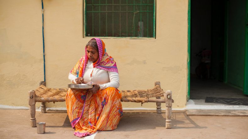 Laxmi eet haar lunch op het stoepje voor haar huis